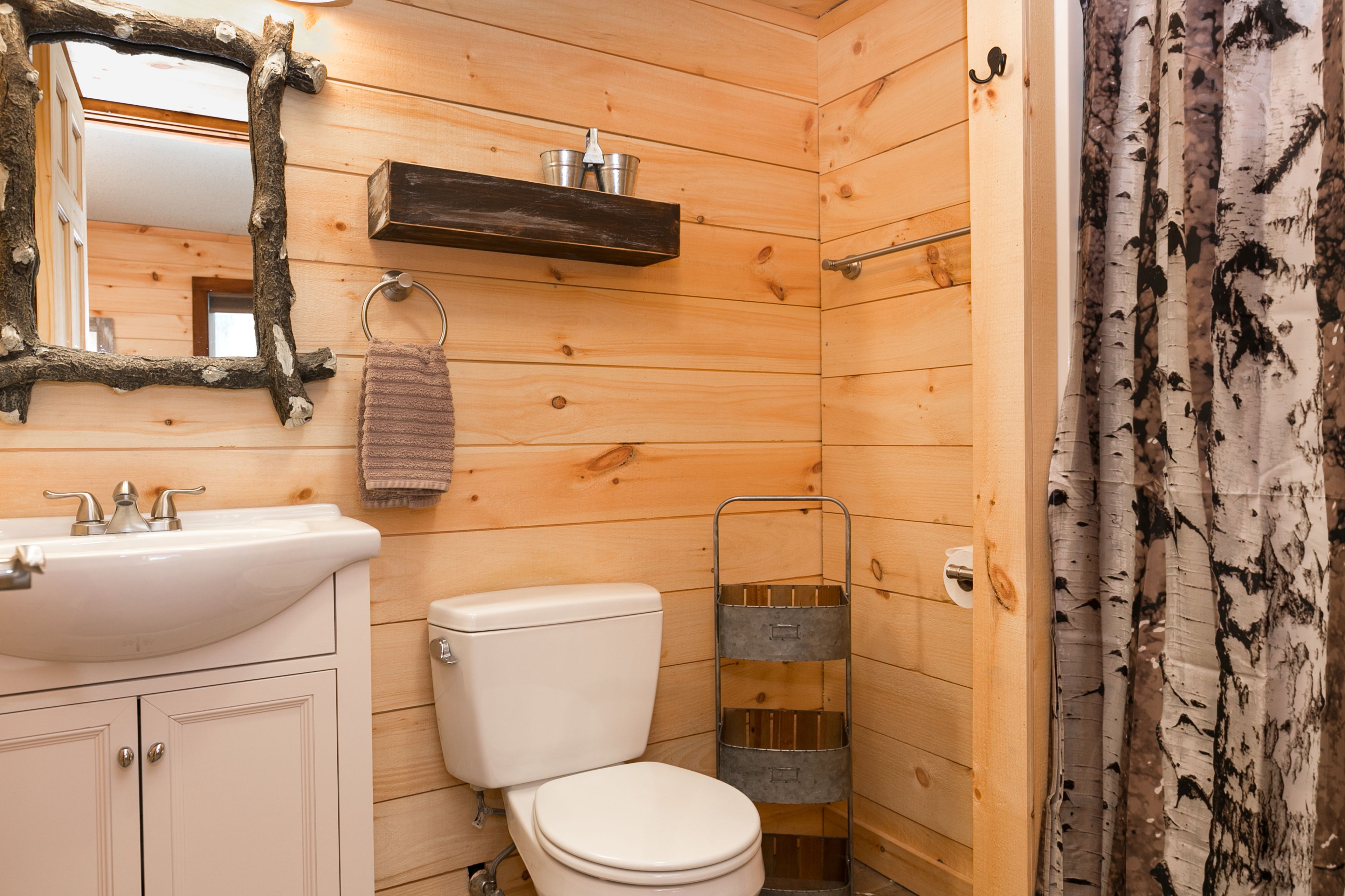 Een houten badkamer met een wit wastafel, toilet en een spiegel met een rustieke lijst.