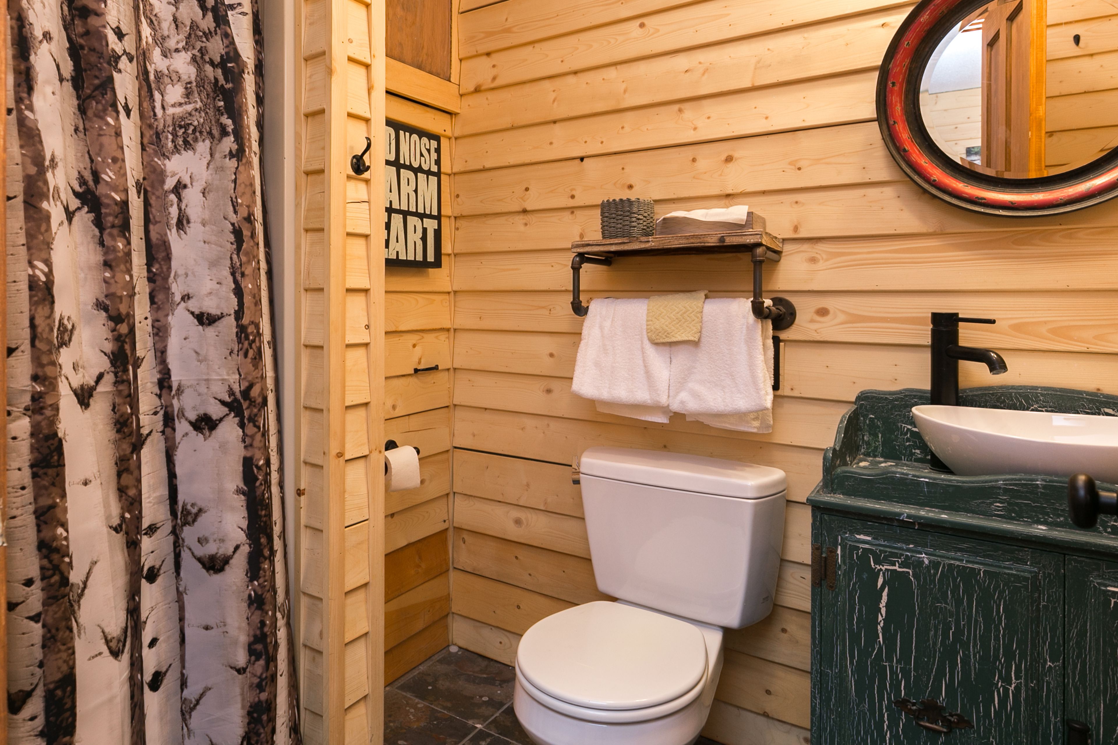 A wooden bathroom with a toilet, sink, and a mirror.