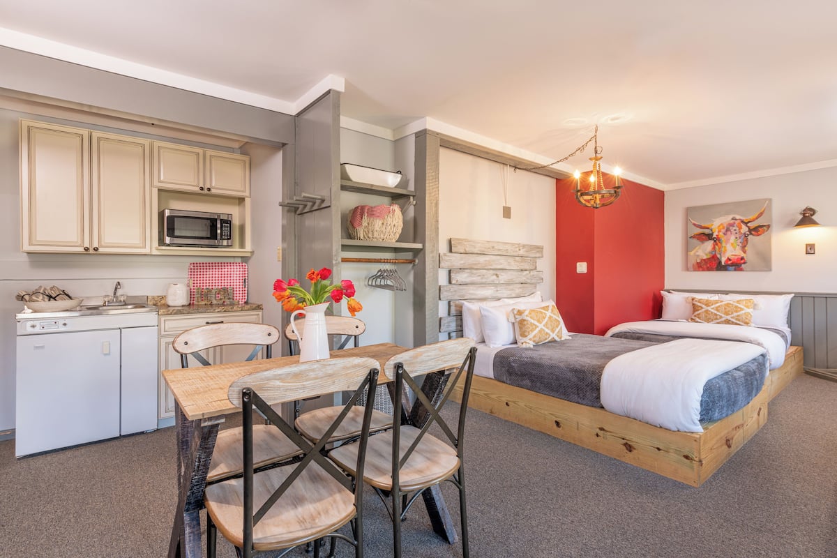 Quarto compacto com cama, mesa de jantar com cadeiras, cozinha compacta e uma parede com destaque vermelha.