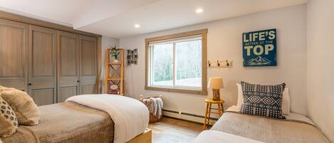 Un dormitorio con dos camas, un armario de madera, una ventana con vistas y una obra de arte con mensajes motivadores.
