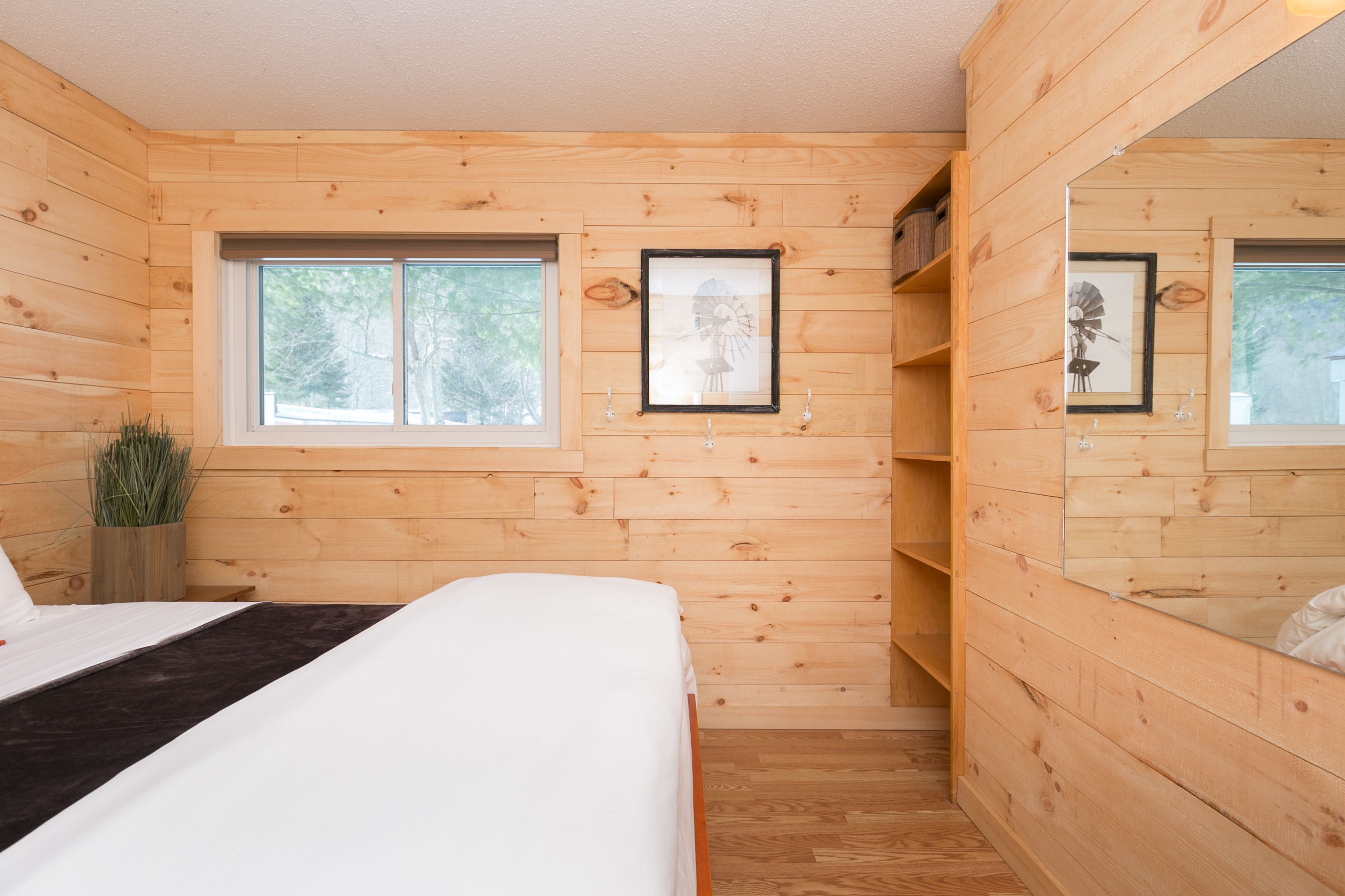 A wooden cabin room with a bed, a window, and a shelf with framed pictures.