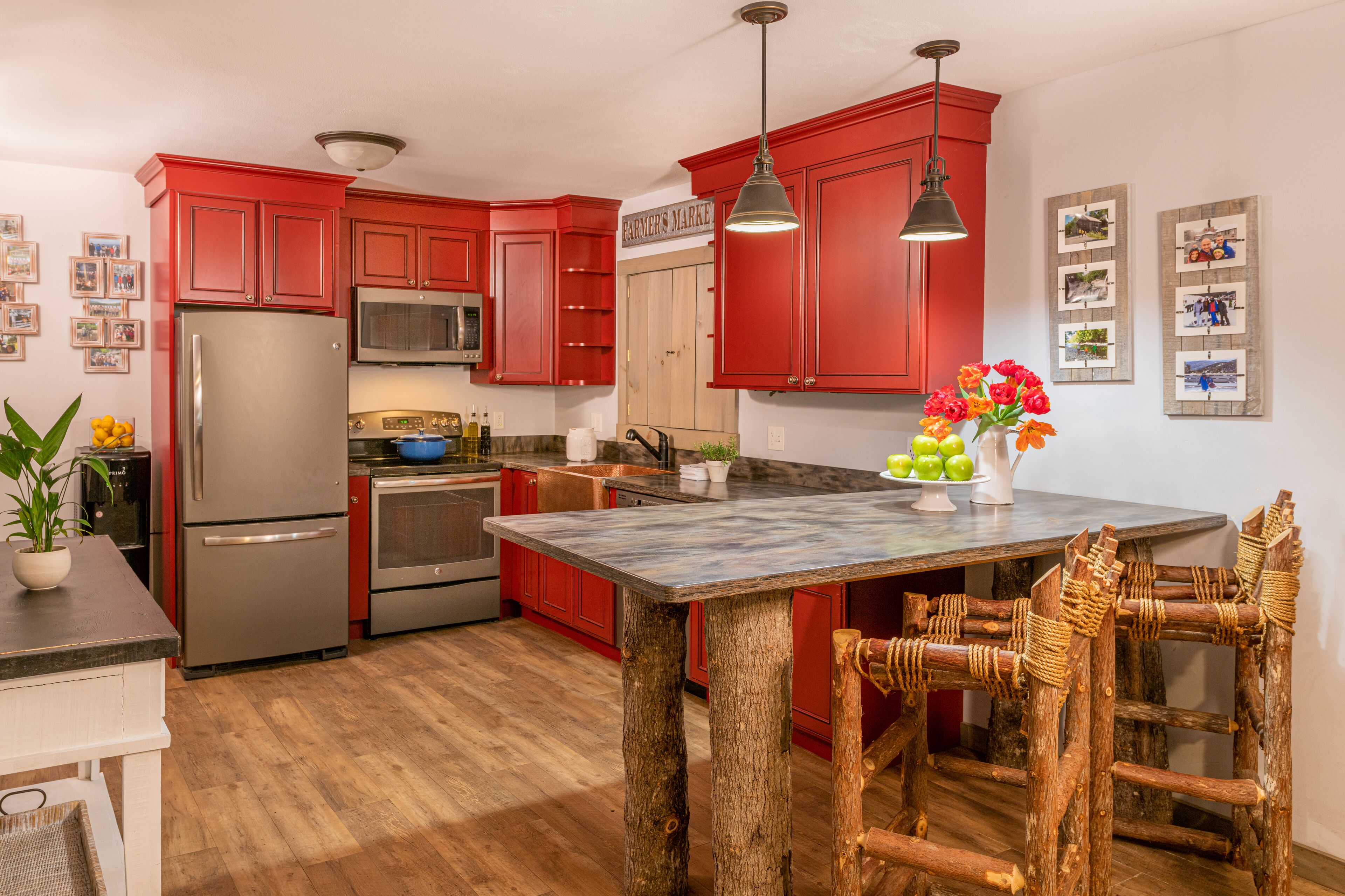 Una cocina con armarios rojos, electrodomésticos de acero inoxidable, una isla de madera y sillas de mimbre.