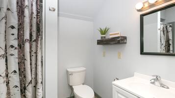 Une salle de bain comprenant des toilettes, un lavabo, un miroir et une étagère sur laquelle est posée une plante.