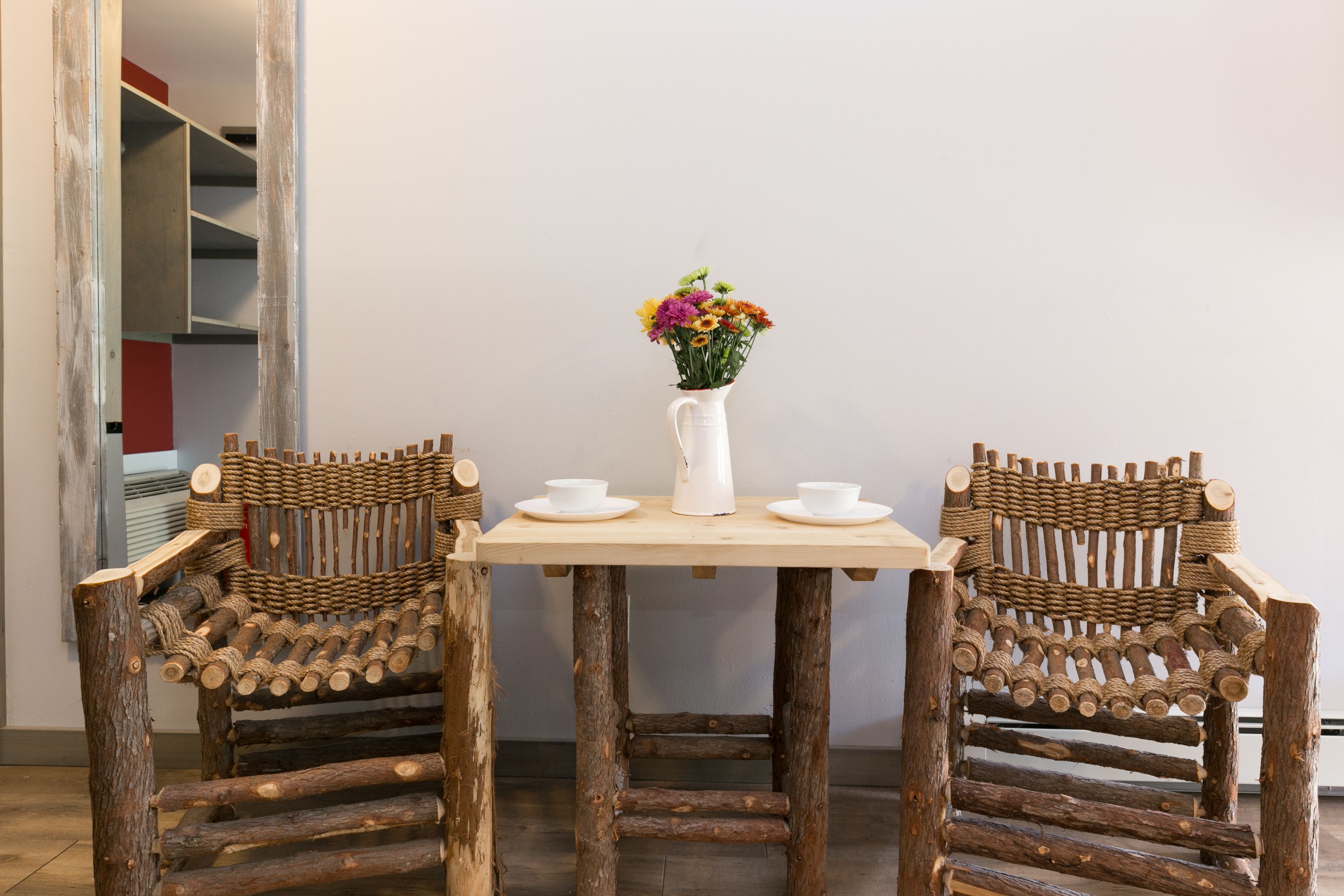 Uma mesa de madeira rústica com duas cadeiras, um jarro branco e um vaso de flores.