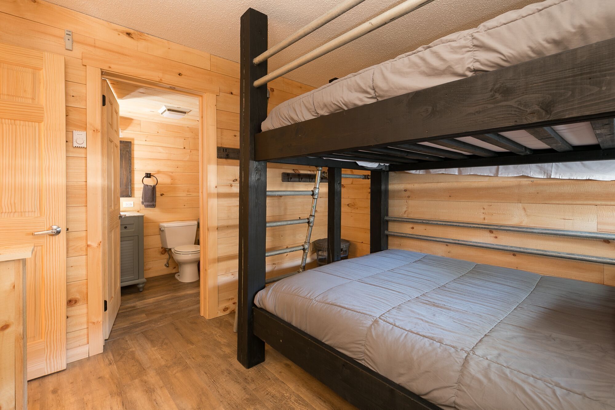 A bunk bed room with wooden walls, a toilet, and a small window.