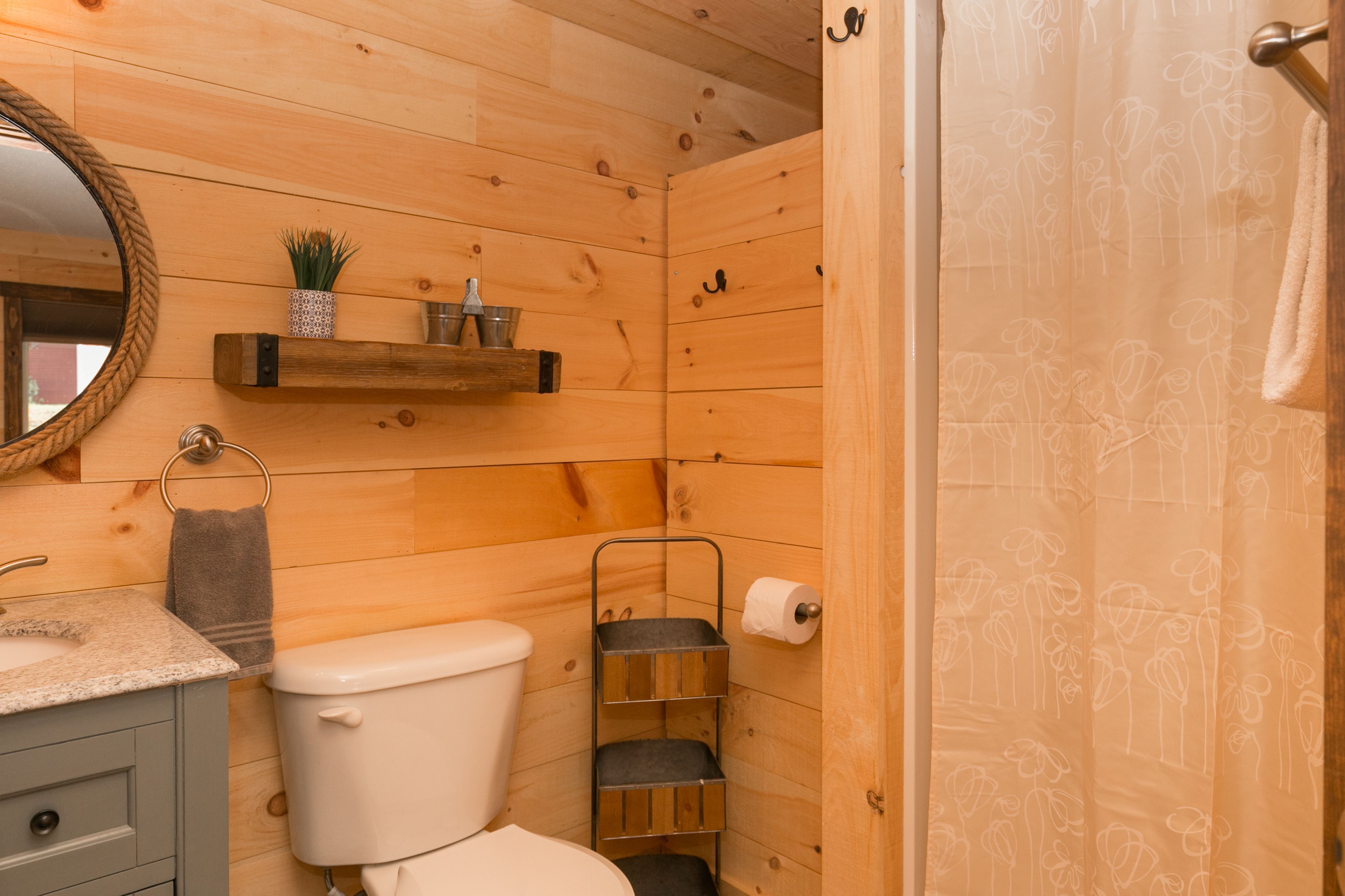 A wooden cabin bathroom with a toilet, sink, and a shelf with toiletries.