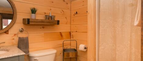 A wooden cabin bathroom with a toilet, sink, and a shelf with toiletries.
