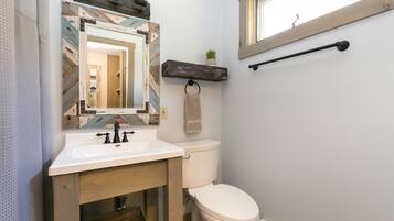 A bathroom with a white sink, wooden vanity, a toilet, a mirror with a decorative frame, a towel rack, and a small plant on a shelf.