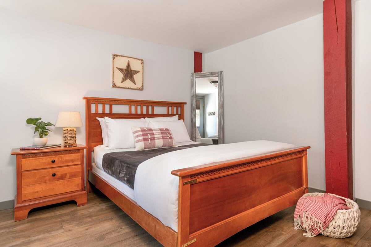 Uma cama de madeira com cabeceira, uma mesa de cabeceira com abajur e uma decoração de estrela na parede.