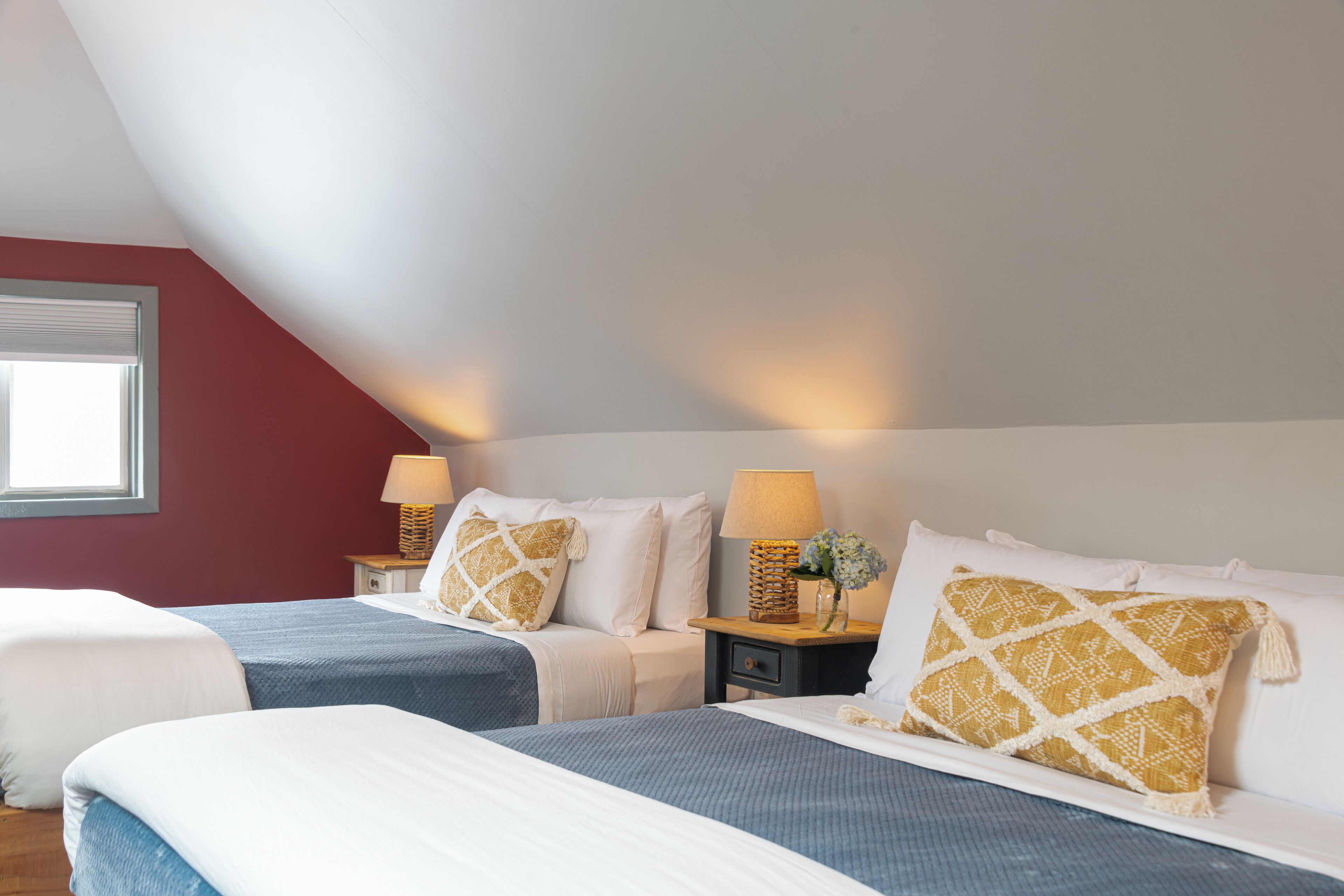 A bedroom with two beds, a window, and two bedside tables with lamps and decorative items.