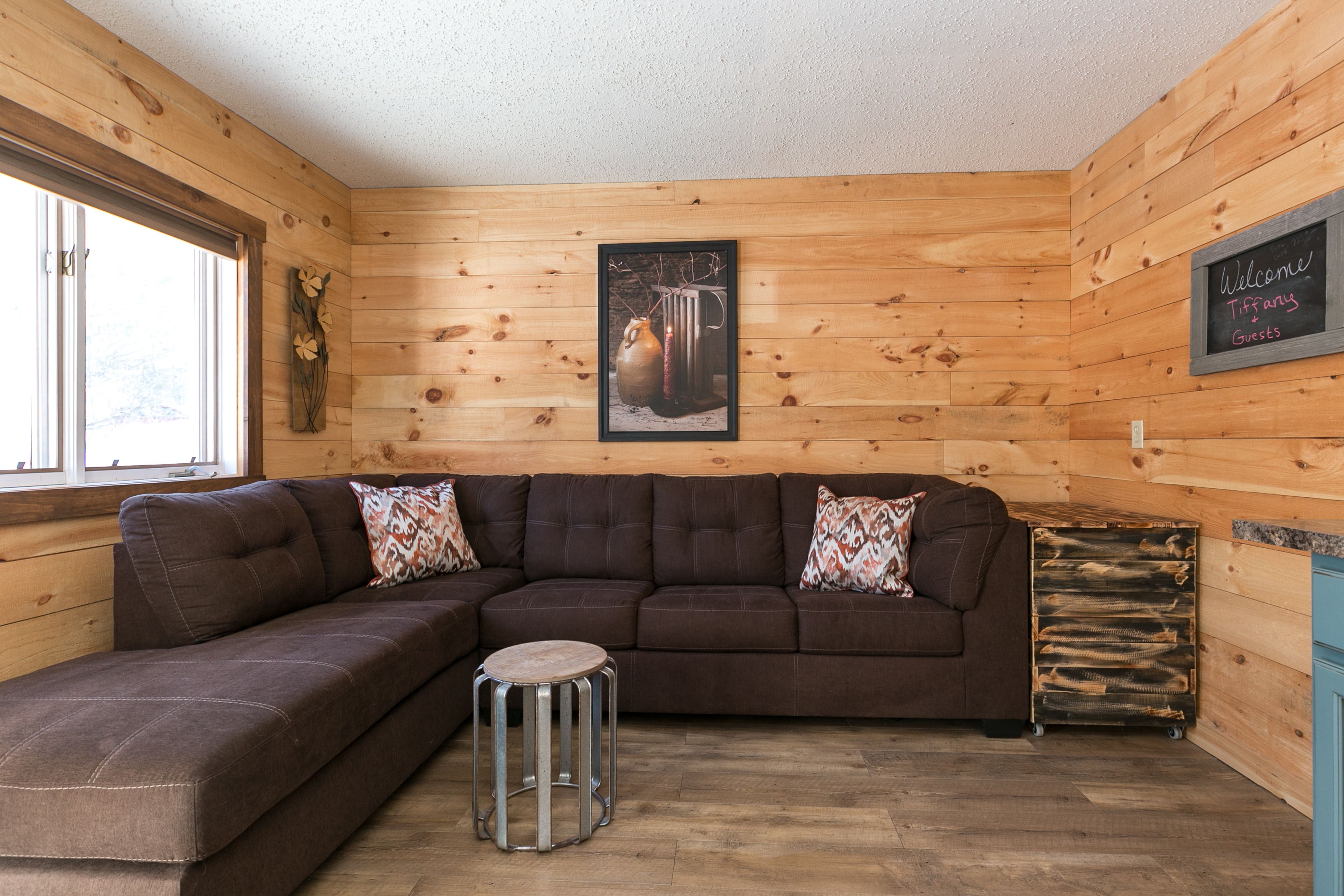 Ein gemütliches Zimmer mit einer Eckcouch, einem kleinen Hocker und einem gerahmten Bild an der Wand.
