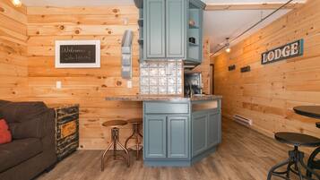 Una habitación acogedora de estilo cabaña con paredes de madera, kitchenette, un sofá marrón y un cartel que dice 'Welcome Shikermo'.