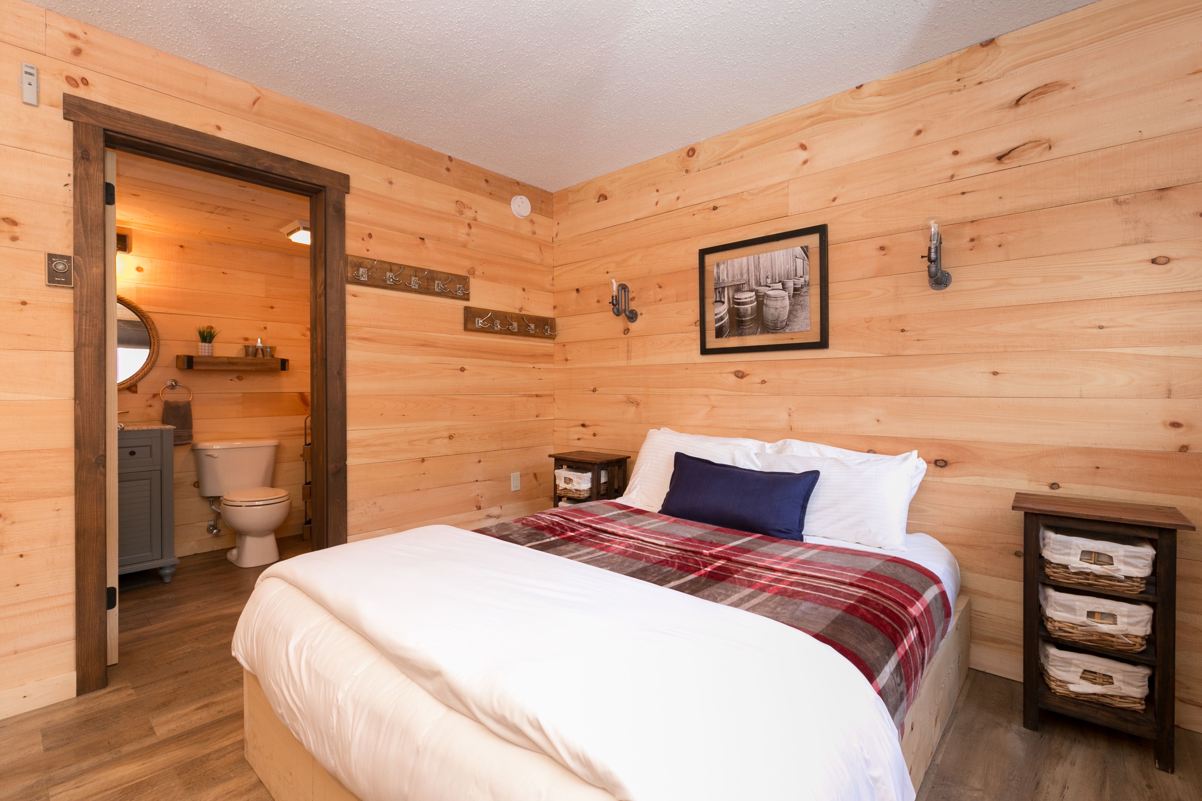 A wooden-paneled bedroom with a bed, a nightstand, a framed picture, and a wooden cabinet.