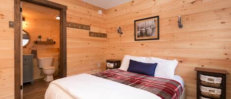 A wooden-paneled bedroom with a bed, a nightstand, a framed picture, and a wooden cabinet.