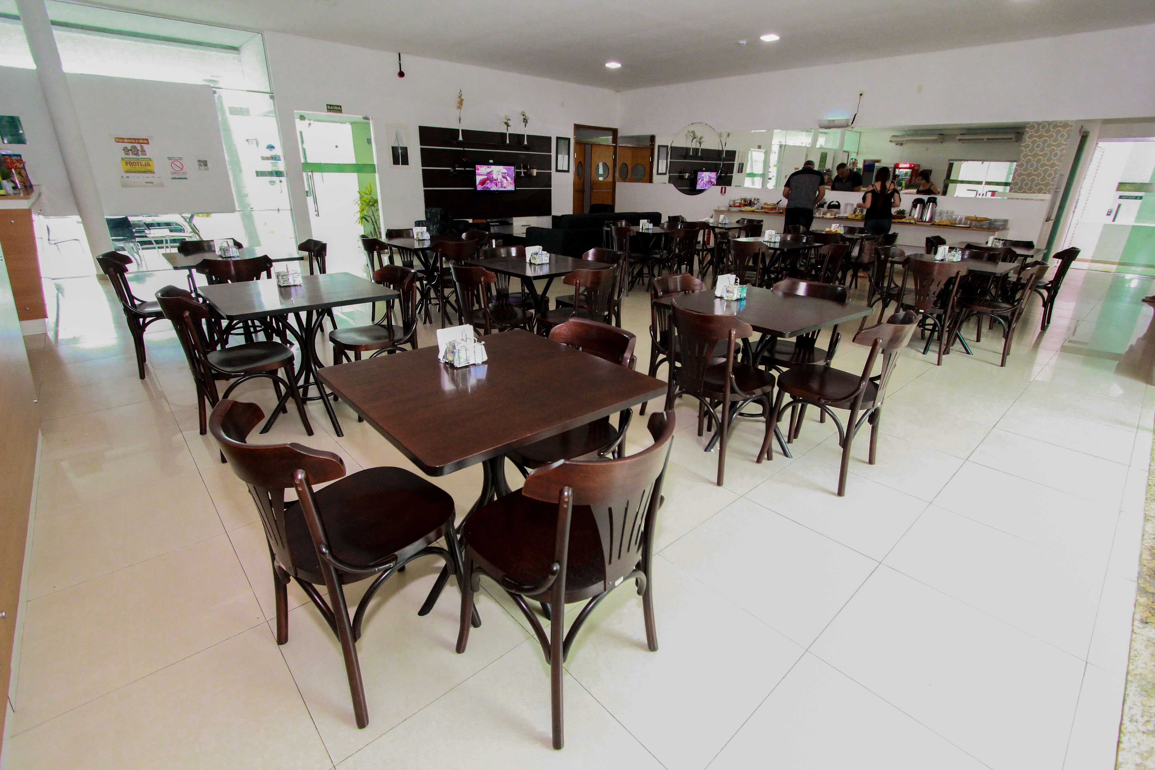Un comedor amplio con varias mesas y sillas, una cocina al fondo, y un ventanal que proporciona luz natural.