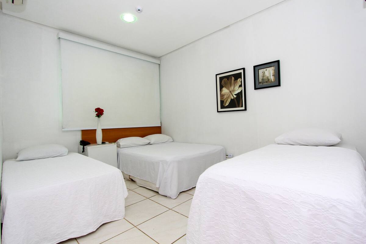A hotel room with two single beds, a small bedside table with a vase of flowers, and two framed pictures on the wall.