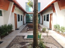 Un edificio moderno con un patio central, que incluye una palmera, una zona de estar y diversas plantas.