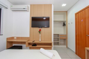Habitación de hotel con cama, televisor montado en la pared, escritorio de madera, una mesita, armario y puerta con letrero de no fumar.