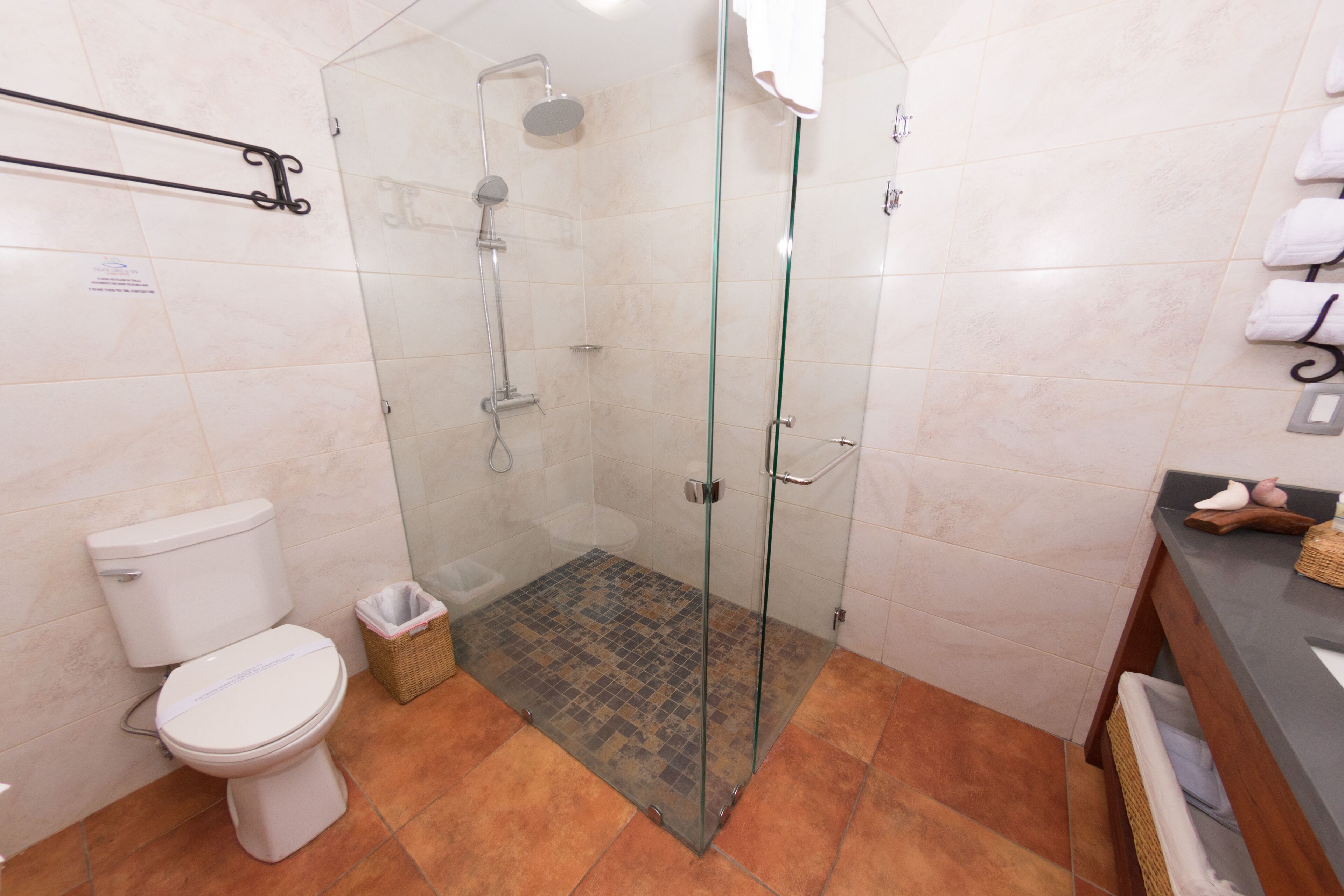 Un baño con ducha de mampara de vidrio, inodoro y zona de lavamanos con toallas y una cesta.