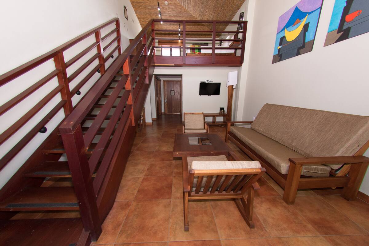 Ein geräumiger Wohnbereich mit einer Holztreppe, einem Sofa, einem Couchtisch und einem an der Wand befestigten Fernseher.