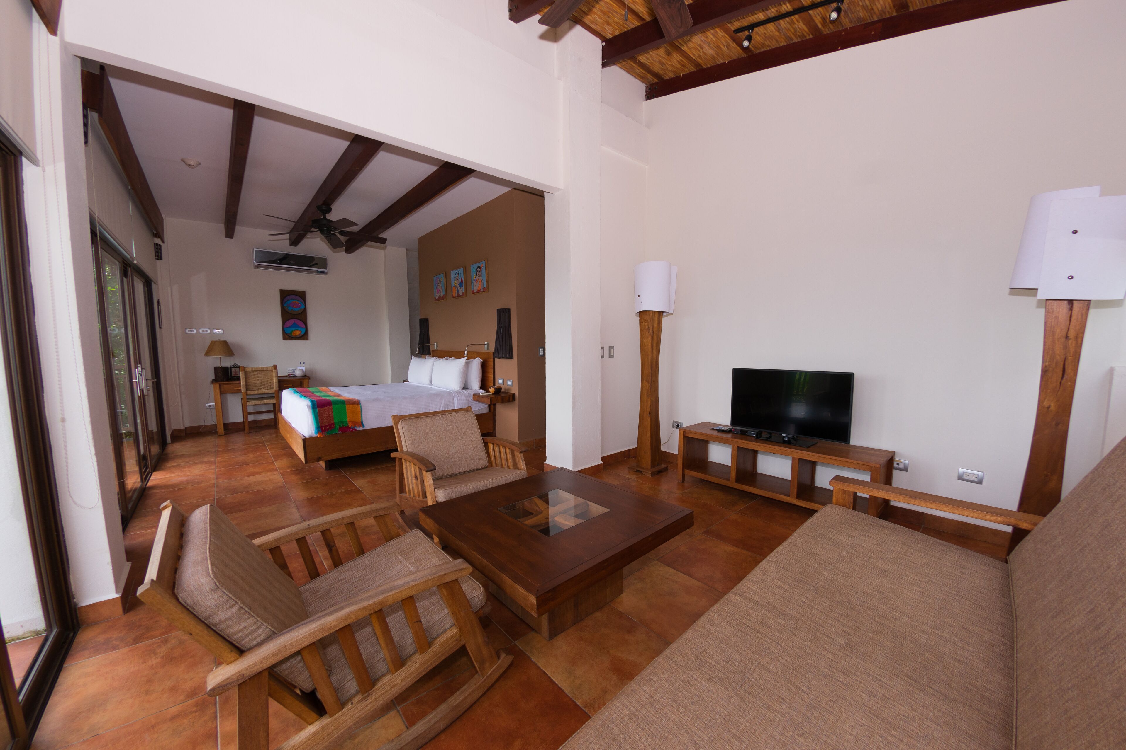 A spacious living area with a sofa, chairs, a coffee table, a TV, and a bed in the background.
