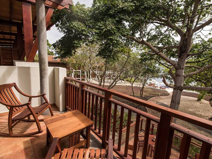 Une terrasse en bois avec une table et des chaises, donnant sur un espace aménagé avec des arbres et offrant une vue sur un bâtiment en arrière-plan.