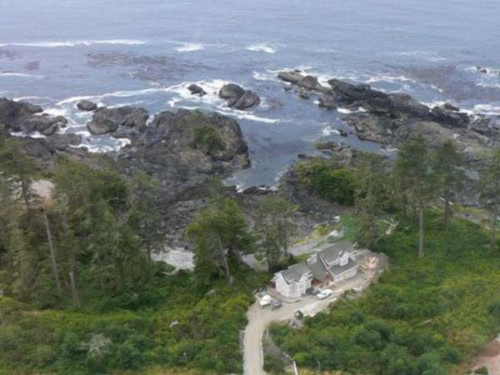 A coastal property with a rocky shoreline, dense greenery, and a few houses.