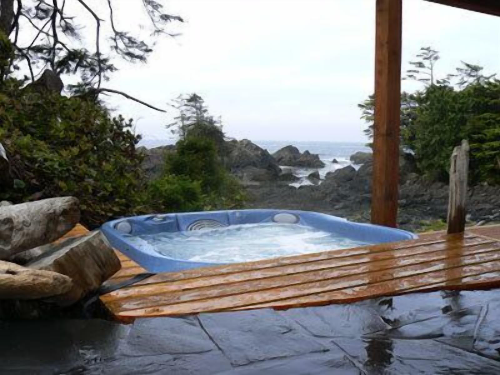 A hot tub on a wooden deck with a rocky landscape and ocean view.