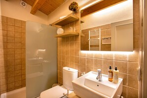 A bathroom with a bathtub, toilet, sink, and a mirror. There are wooden shelves above the sink and a shower with a glass door. - Hotel Boutique Niu Del Sol (Palau-Saverdera)