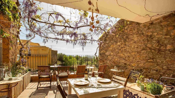 An outdoor patio with stone walls, wooden furniture, and hanging plants. - Hotel Boutique Niu Del Sol (Palau-Saverdera)