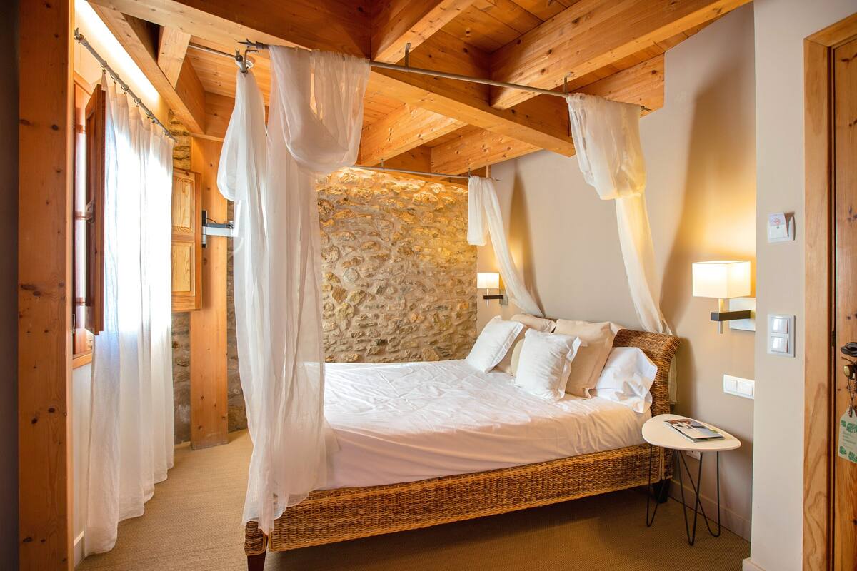 A bedroom with a stone wall, a canopy bed, and a small bedside table.