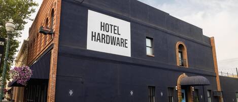 A building with a sign reading "HOTEL HARDWARE" and a parking lot in front.