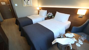 Ein Hotelzimmer mit zwei Betten, einem Esstisch mit Stuhl, einem kleinen Tisch mit Glas und Servette sowie einer Wandlampe.