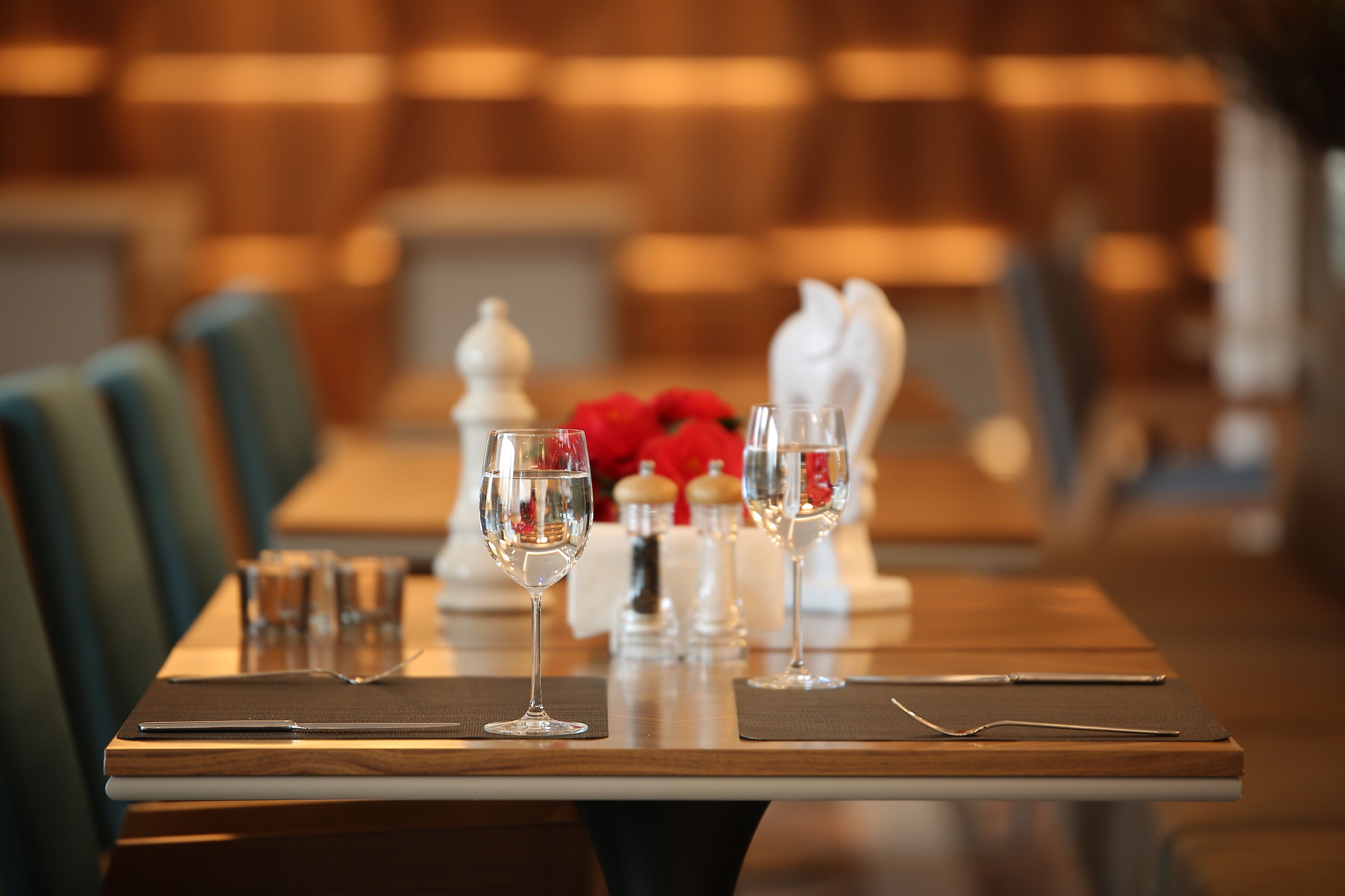 A dining table set with wine glasses, a knife, and a spoon, with a vase of red flowers in the background.