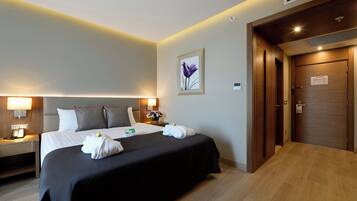 Une chambre d’hôtel avec un lit, des lampes de chevet, une table de chevet, un tableau encadré et une porte en bois.