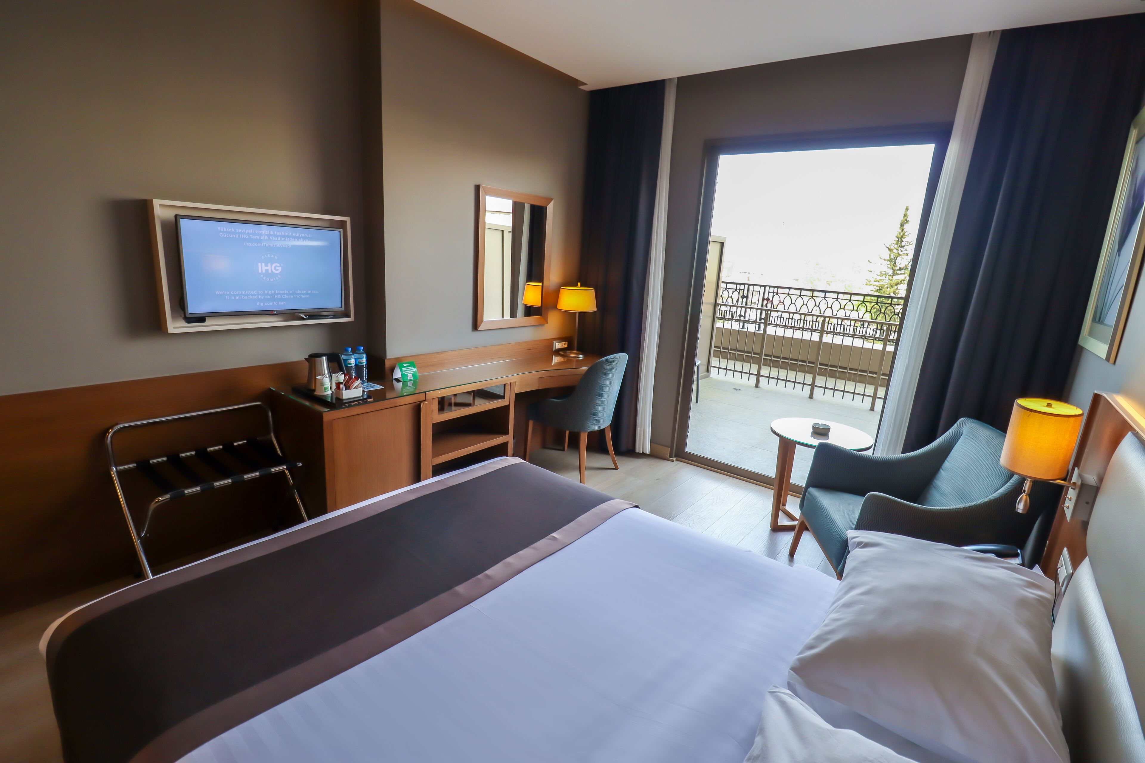 Une chambre d’hôtel équipée d’un lit, d’un bureau, d’une chaise, d’une télévision et d’un balcon avec une balustrade.