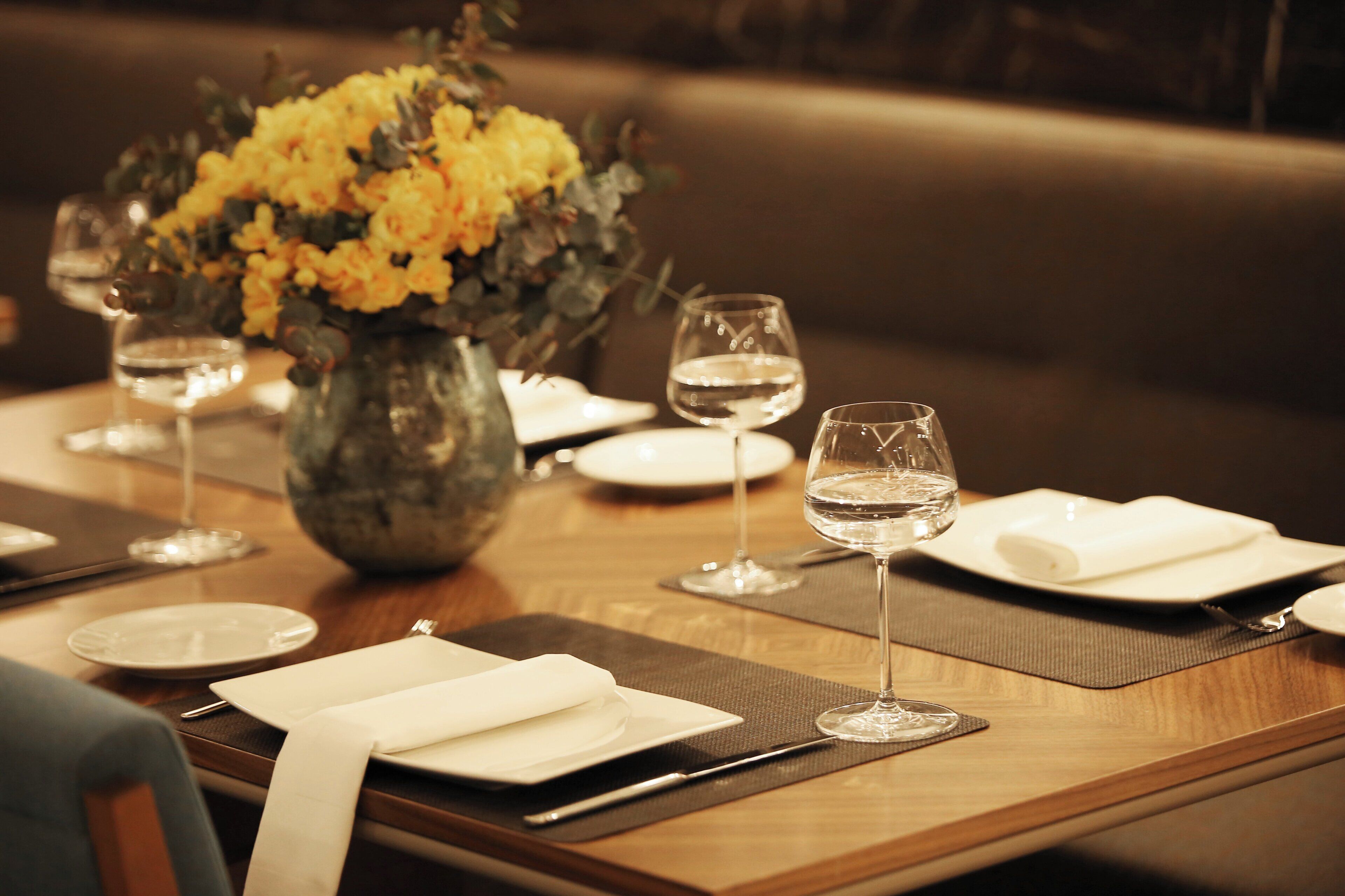 A dining table set with plates, glasses, and a vase of flowers.