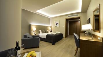 Habitación de hotel con cama, escritorio, silla, sofá y mesa de comedor con fruta y una botella de vino.