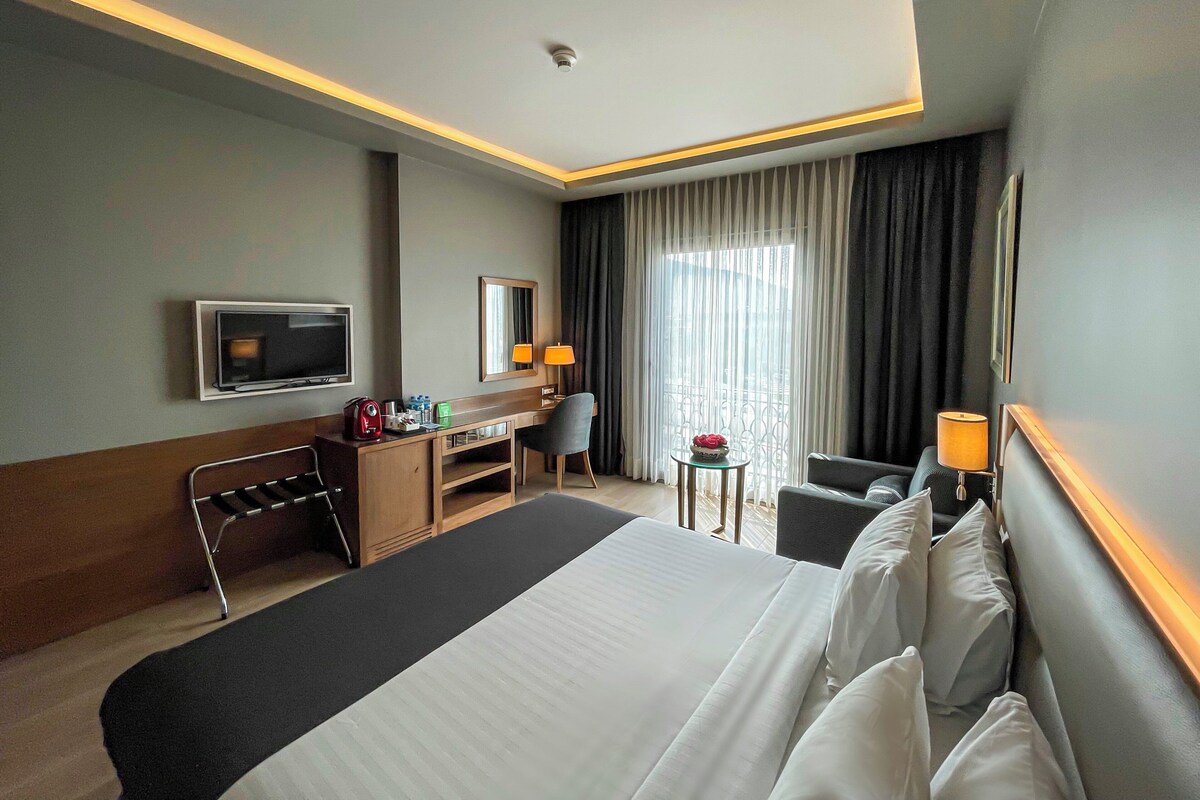 Une chambre d’hôtel avec un grand lit, un bureau, une chaise, une télévision et une fenêtre avec des rideaux.