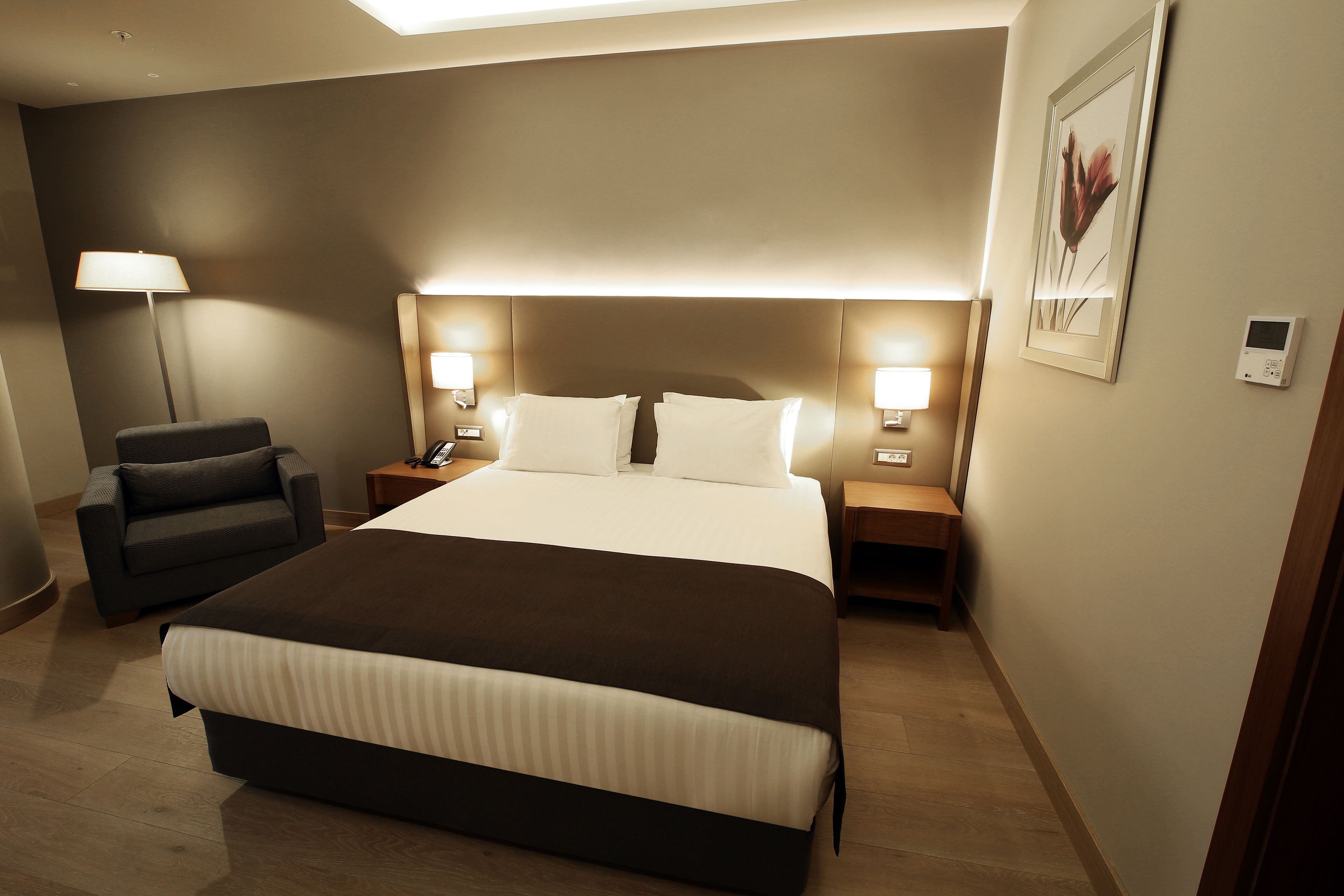 A hotel room with a large bed, bedside tables, a lamp, and a chair.