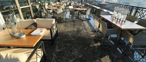 Una terraza en la azotea con mobiliario exterior, vistas a la ciudad y suelo de mármol.