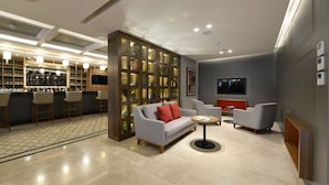 Un espace de vie moderne comprenant un canapé, des fauteuils, une table basse et un bar avec des tabourets.