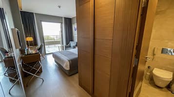 A hotel room with a bed, a desk with a chair, a wardrobe, and a bathroom with a toilet.
