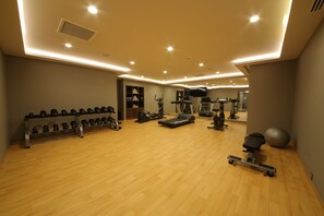 Une salle de sport spacieuse équipée de divers appareils d’exercice, notamment des tapis de course, des poids et un rameur.