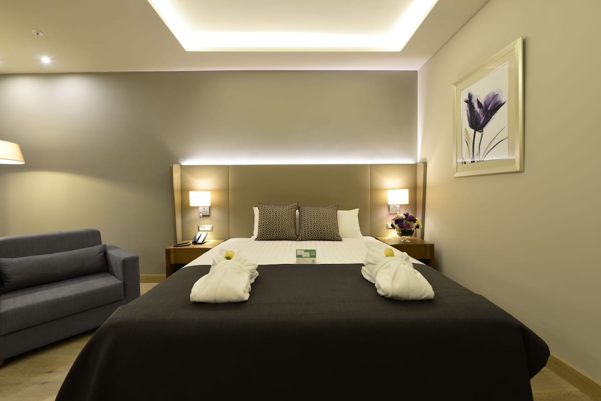 Ein Hotelzimmer mit Bett, Nachttischlampen, einem Nachttisch, einer Couch und einem gerahmten Bild an der Wand.