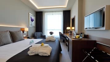 Habitación de hotel con una cama grande, un escritorio, una silla, un televisor y una ventana con cortinas.