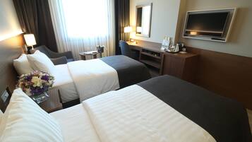 Een hotelkamer met twee bedden, een bureau, een stoel, een televisie en een raam met gordijnen.