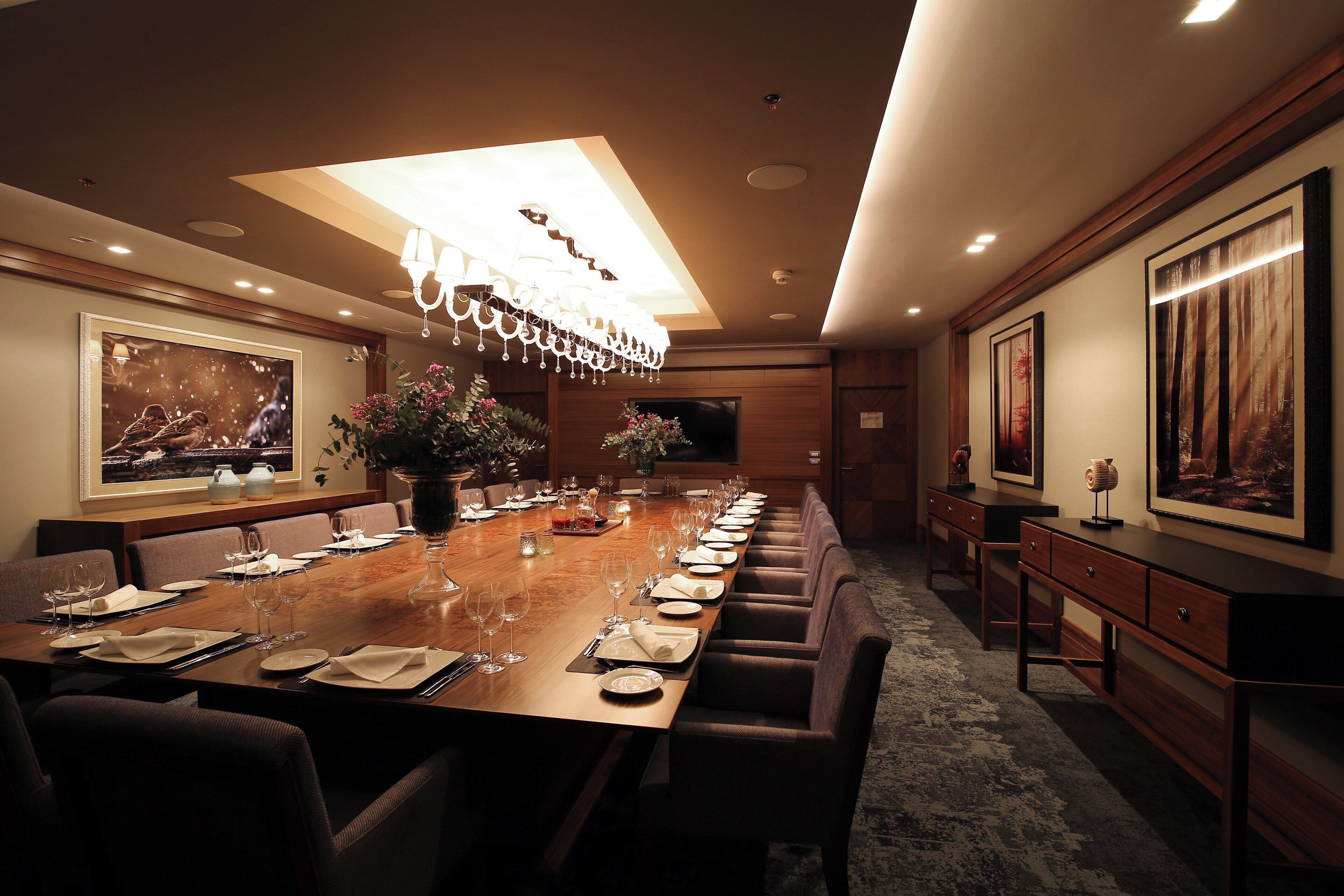 A long dining table set for a meal with chairs, a chandelier, and artwork on the walls.