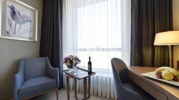Ein Hotelzimmer mit zwei Sesseln, einem kleinen Tisch mit Blumen, einer Weinflasche und einer Obstplatte.