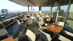 Une terrasse sur le toit, aménagée avec des meubles en osier, des garde-corps en verre et offrant une vue sur la ville.